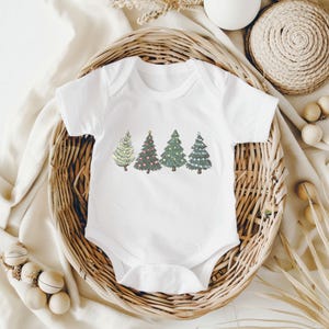 May include: White baby bodysuit with a festive Christmas tree design. The design features four different trees in shades of green, with lights and ornaments. The bodysuit is made of soft material and is perfect for the holiday season.