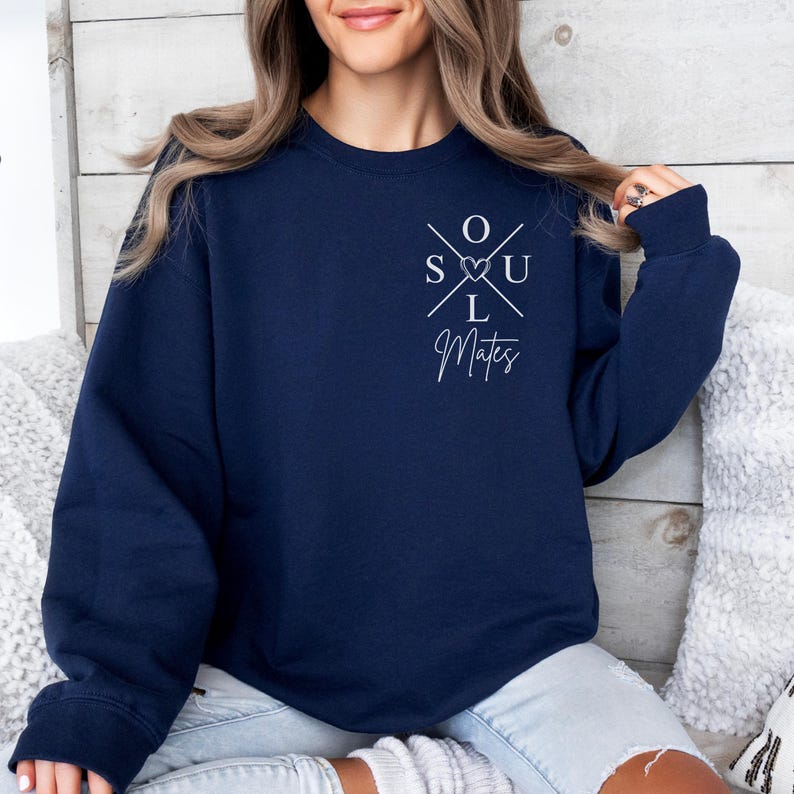May include: A navy blue crew neck sweatshirt. The front features the white text "SOUL Mates" in a cross design with a heart symbol. The sweatshirt is a dark blue colour.