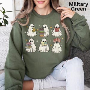 May include: Military green sweatshirt featuring a design of six cartoon ghosts reading books. The ghosts are white with black eyes and are holding stacks of books or reading from them. The design includes yellow stars.