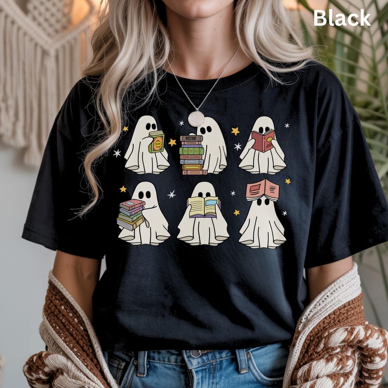 May include: Black t-shirt featuring a design of six cartoon ghosts reading books. The ghosts are white with black eyes and are surrounded by yellow stars. The word "Black" is printed at the top right of the shirt.