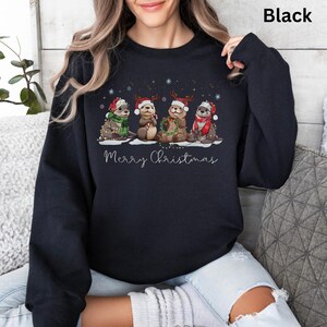 Pu&ograve; includere: Felpa nera con un design a tema natalizio. Presenta quattro lontre con cappelli e sciarpe festosi, che tengono oggetti natalizi. Le parole "Merry Christmas" sono scritte sotto le lontre in un carattere script. Sono presenti anche fiocchi di neve.