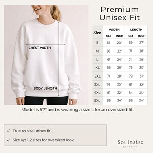 May include: A white unisex sweatshirt with chest width and body length measurements. The image includes a size chart with measurements in inches and centimeters. The model is 5'7" and wearing a size L for an oversized fit. The text says "Premium Unisex Fit".