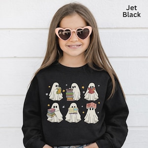 Può includere: Felpa nera con una grafica di sei fantasmi dei cartoni animati che leggono libri. I fantasmi sono bianchi con occhi neri e sono circondati da piccole stelle gialle. Il testo "Jet Black" si trova nell'angolo in alto a destra.