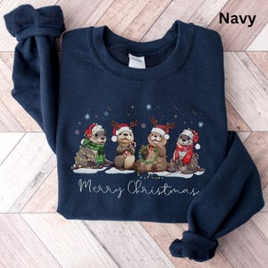 Pu&ograve; includere: Felpa blu navy con un design natalizio. Quattro lontre indossano cappelli e sciarpe di Babbo Natale, decorate con luci. La scritta "Merry Christmas" &egrave; in basso. La parola "Navy" &egrave; stampata in alto a destra.