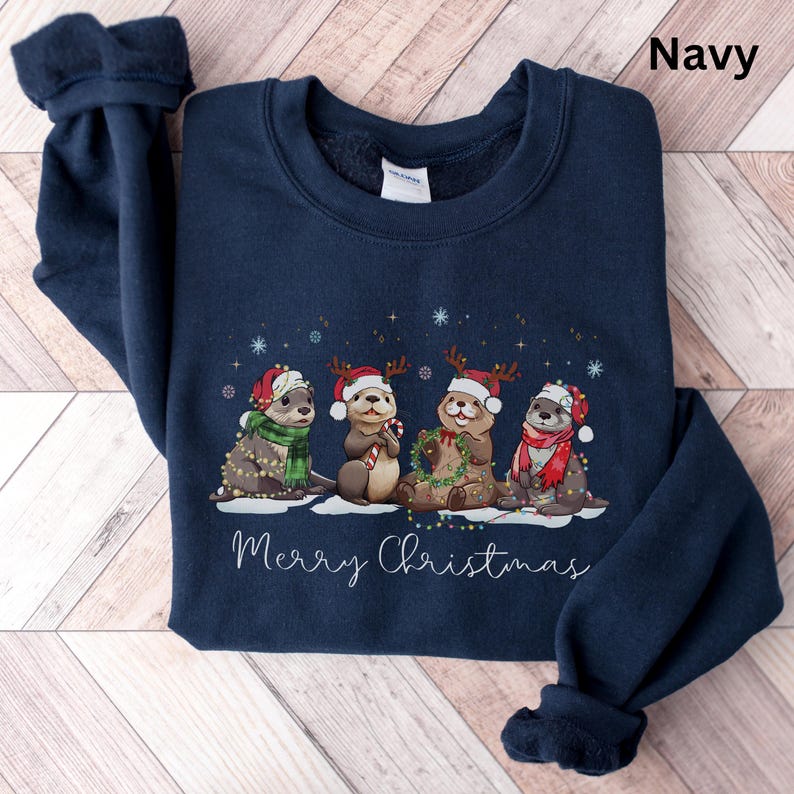 Pu&ograve; includere: Felpa blu navy con un design natalizio. Quattro lontre indossano cappelli e sciarpe di Babbo Natale, decorate con luci. La scritta "Merry Christmas" &egrave; in basso. La parola "Navy" &egrave; stampata in alto a destra.