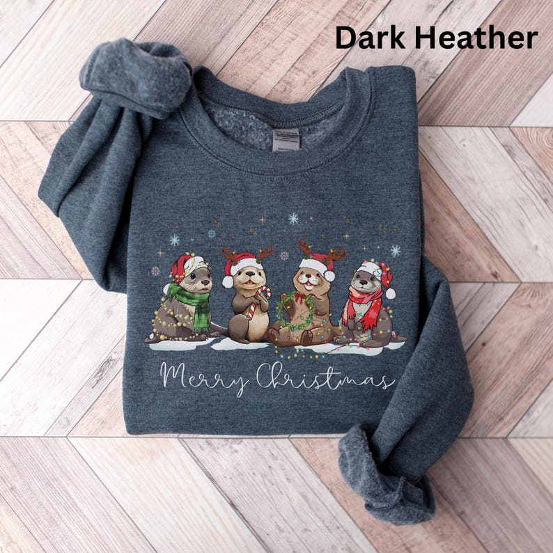 Pu&ograve; includere: Felpa grigio scuro con un design natalizio con le lontre. L'illustrazione mostra quattro lontre con cappelli e sciarpe di Babbo Natale, con la scritta "Merry Christmas" sotto. Le lontre sono decorate con luci natalizie e bastoncini di zucchero.