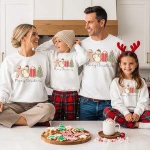 May include: White crewneck sweatshirts with a Christmas theme. Each sweatshirt features a gingerbread man, snowman, gift, and Christmas tree design, with "Merry Christmas" text. The family is wearing matching outfits.