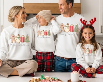 Op de afbeelding: Witte crewneck sweatshirts met een kerstthema. Elke sweatshirt heeft een peperkoeken man, sneeuwpop, cadeau en kerstboom ontwerp, met de tekst "Merry Christmas". De familie draagt bijpassende outfits.