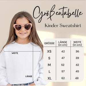 Puede incluir: Una persona joven con una sudadera blanca y gafas de sol en forma de coraz&oacute;n. La imagen incluye una tabla de tallas en alem&aacute;n, con medidas en cent&iacute;metros para largo y ancho. Tambi&eacute;n se ve el texto "Kinder Sweatshirt".