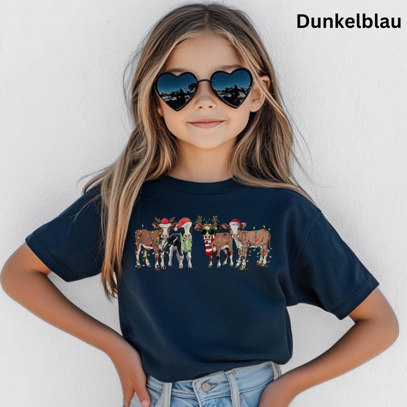 Puede incluir: Una camiseta azul marino con un dise&ntilde;o navide&ntilde;o de vacas vestidas con atuendos festivos. Las vacas est&aacute;n adornadas con gorros de Pap&aacute; Noel, cuernos de reno y luces de cadena. El texto "Dunkelblau" est&aacute; impreso en la parte superior.