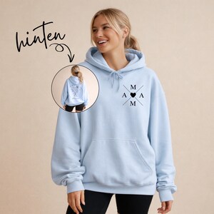May include: A light blue hoodie with a front pocket and a hood. The hoodie features a black graphic with the letters "M", "A", and a heart symbol. The word "hinten" is written in black script above a smaller image of the hoodie.