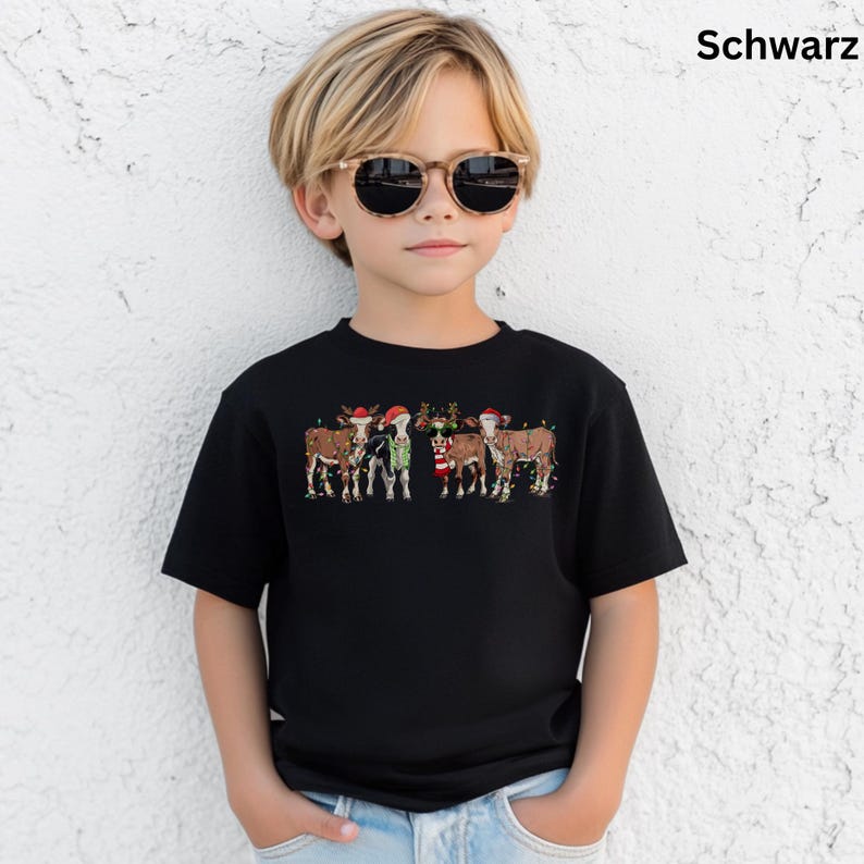 Puede incluir: Camiseta negra con un dise&ntilde;o festivo de vacas con gorros de Pap&aacute; Noel y decoraciones navide&ntilde;as. La palabra "Schwarz" est&aacute; impresa en la esquina superior derecha. La camiseta la lleva un ni&ntilde;o con gafas de sol.