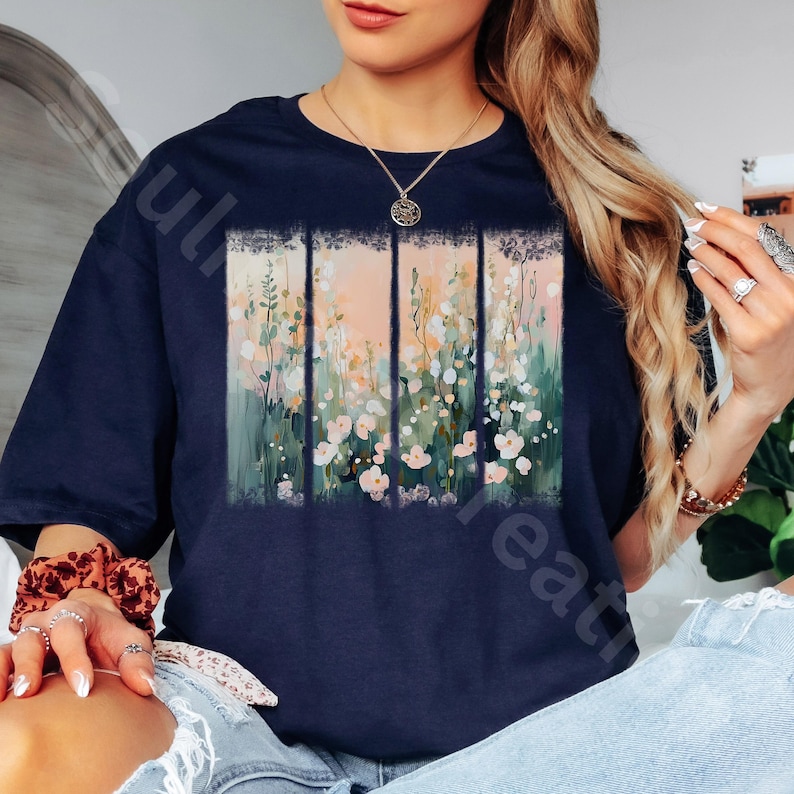 May include: Navy blue t-shirt featuring a floral design. The artwork is divided into four vertical panels with a pastel color palette of pink, green, and white flowers. The shirt has short sleeves and a relaxed fit.
