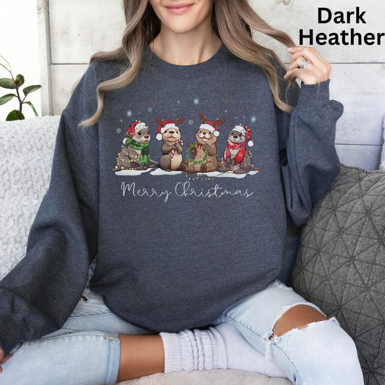 Pu&ograve; includere: Felpa grigio scuro con un design natalizio. La grafica mostra quattro lontre con cappelli e sciarpe festive, con la scritta "Merry Christmas" sotto. Le lontre sono decorate con ornamenti natalizi. Un capo d'abbigliamento comodo e stagionale.