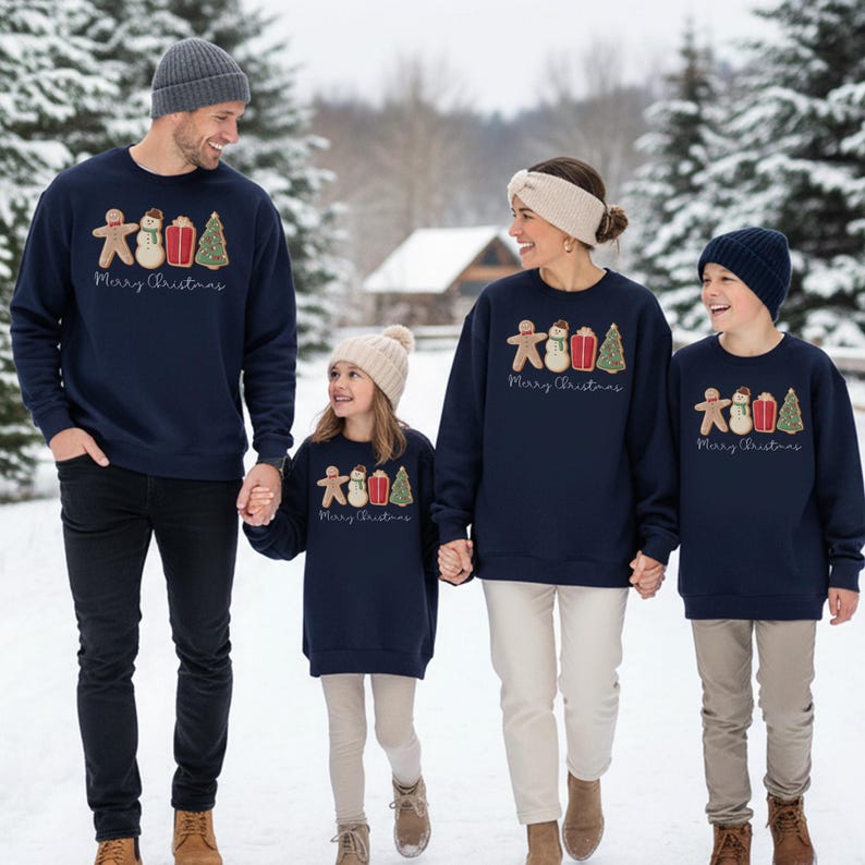 May include: A family of four wearing matching navy blue sweatshirts with a Christmas design. The design includes a gingerbread man, snowman, gift, and Christmas tree. The words "Merry Christmas" are printed below the design.