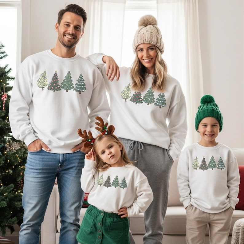 May include: White sweatshirts with a Christmas tree design. The sweatshirts are worn by a family of four. The Christmas tree design includes green, red, and gold colors. The family is standing in front of a Christmas tree.