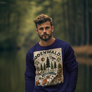 Könnte beinhalten: Ein marineblauer Pullover mit einem grafischen Aufdruck einer Waldszene. Der Aufdruck zeigt Bäume, Pilze, Eulen und Füchse. Der Text "ODENWALD" erscheint zweimal im Aufdruck.