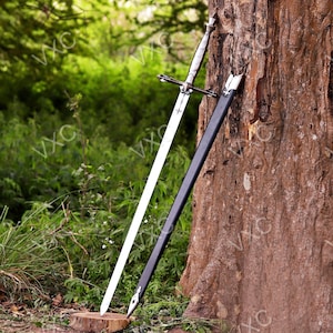 May include: A long, silver and steel sword with a white blade, resting against a tree. The sword has a cross-shaped hilt and is accompanied by a black sheath. The background features lush green foliage.
