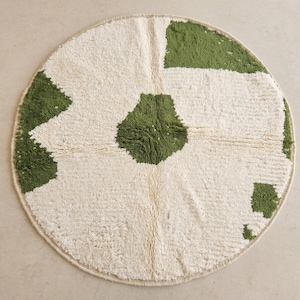 Puede incluir: Alfombra redonda con fondo blanco y formas geométricas verdes. La alfombra tiene un aspecto suave y texturizado, con un diseño sencillo y moderno. Adecuada para salón o dormitorio, mide unos 120 cm de diámetro.