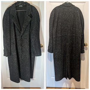 May include: A long, charcoal gray overcoat featuring a speckled white pattern throughout the fabric. The coat has a notched lapel, a button-front closure, long sleeves with cuff tabs, and a horizontal seam across the back with a center vent.