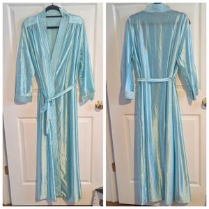 May include: A light blue, full-length robe with a matching belt. The robe has a shiny, pleated texture and striped accents on the collar and cuffs. It is hanging on a black hanger against a white door.