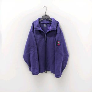 May include: A purple fleece pullover with a quarter-zip neckline and a high collar. The garment features a small rectangular patch on the left sleeve with the letters LT in white, and a GAP brand label is visible on the inner collar area.