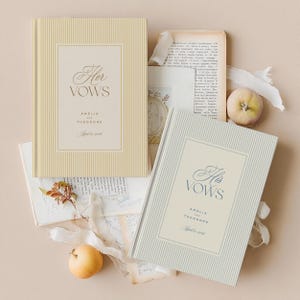 K&ouml;nnte beinhalten: Zwei Hochzeitsgel&uuml;bde-B&uuml;cher mit gestreiften Einb&auml;nden. Eines ist cremefarben mit goldenem Text "Her Vows" und das andere hellgrau mit blauem Text "His Vows". Beide B&uuml;cher enthalten die Namen Amelia und Theodore sowie das Datum 8. April 2026.