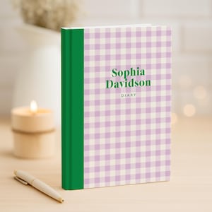 May include: A diary with a light purple and white gingham pattern cover. The spine is green. The text "Sophia Davidson" and "DIARY" are printed in green on the cover. A pen and candle are in the background.
