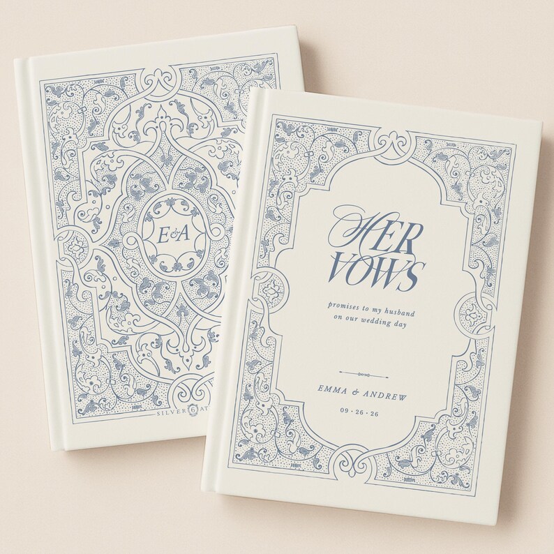 May include: Two off-white wedding vow books with blue floral designs. One book reads "HER VOWS" with the names Emma & Andrew and the wedding date. The other book has the initials "E & A".