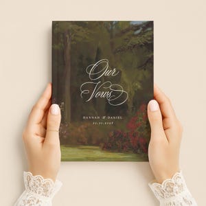May include: A rectangular vow book featuring a dark, painterly forest landscape with deep green trees and red floral accents. The white text reads Our Vows, followed by the names Hannah & Daniel and the date 10.10.2026 in a clean, serif font.