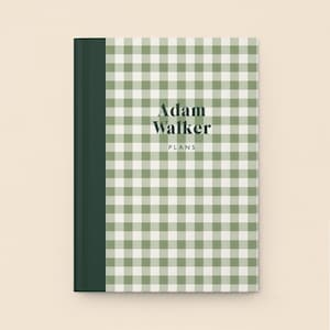May include: A hardcover notebook with a green and white gingham pattern. The spine is a solid dark green. The text "Adam Walker PLANS" is printed in a dark font on the front cover.