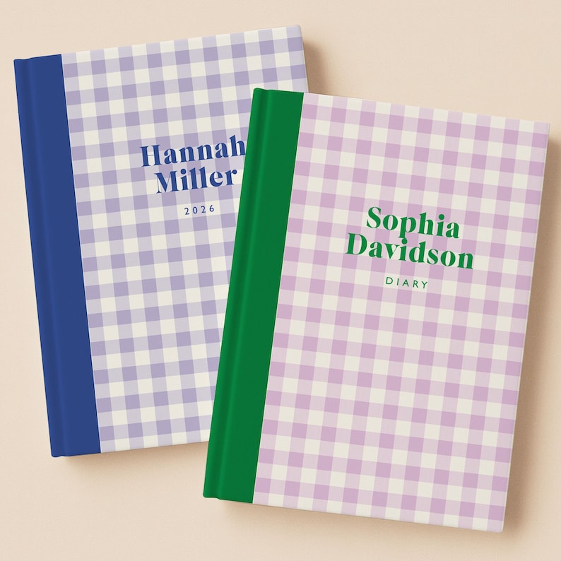 May include: Two hardcover journals with a gingham pattern in lavender and white. One journal has a blue spine and the name "Hannah Miller" and the year "2026" printed on the cover. The other journal has a green spine and the name "Sophia Davidson" and the word "DIARY" printed on the cover.