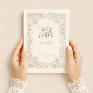 May include: A cream-colored wedding vow book with gold lettering and decorative border. The cover reads "Her Vows" with the names Isabel & Sebastian and the wedding date. The book is held by hands with lace cuffs.