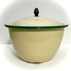 May include: Cream-colored enamelware bowl with a matching lid. The bowl has a green rim and a dark brown knob on the lid. The bowl is a vintage kitchenware item.