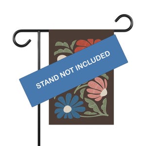 May include: A garden flag featuring a floral pattern in blue, red, and pink on a brown backdrop. The flag is mounted on a black metal stand. The text "STAND NOT INCLUDED" is across the flag.