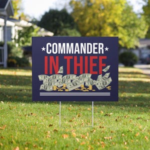 May include: A rectangular yard sign with a dark blue background featuring the white text COMMANDER and red text IN THIEF. Below the text is a graphic illustration of scattered one-hundred-dollar bills and stacks of gold coins on the ground.