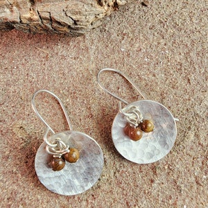 May include: A pair of silver earrings with hammered round discs and brown gemstone accents.