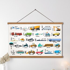 Puede incluir: Un gr&aacute;fico de alfabeto colorido con ilustraciones de diferentes veh&iacute;culos para cada letra. El gr&aacute;fico est&aacute; enmarcado en madera y cuelga de una pared blanca.