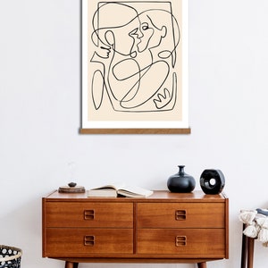 May include: A black and white line drawing of two people embracing, printed on a beige background and framed with a natural wood frame.