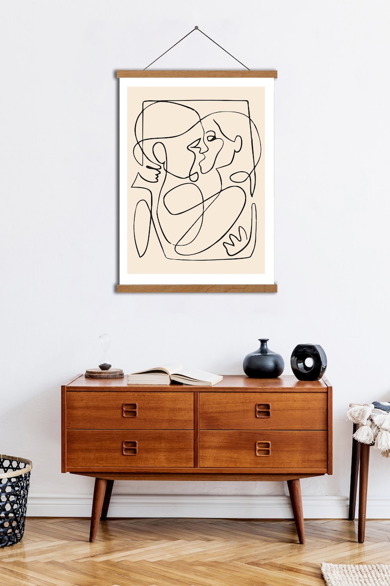May include: A black and white line drawing of two people embracing, printed on a beige background and framed with a natural wood frame.