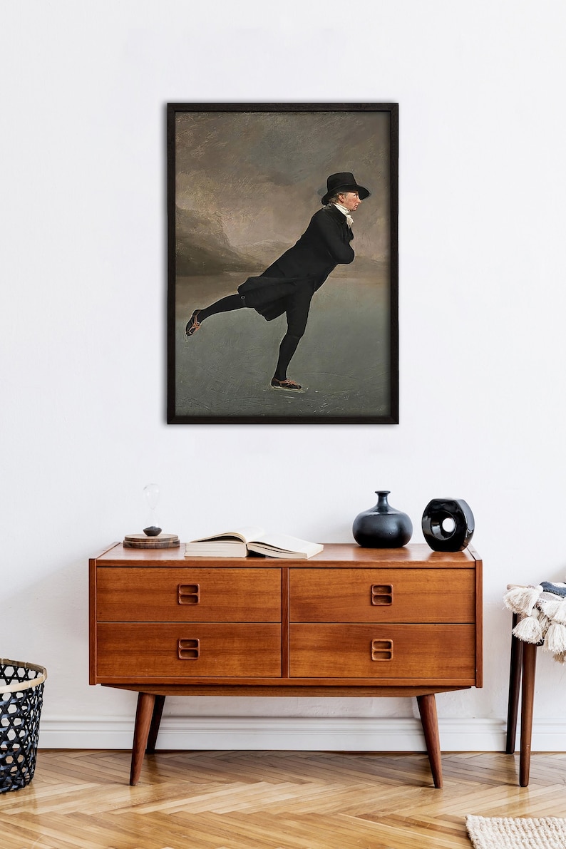 May include: A framed painting depicting a man ice skating on a frozen lake. The man is wearing a black coat, black hat, and black trousers. The background shows a cloudy sky with a mountain range in the distance.