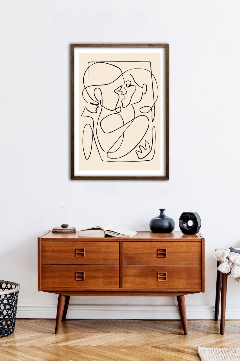 May include: A black and white line drawing of two people embracing, framed in a brown wood frame and hanging on a white wall.