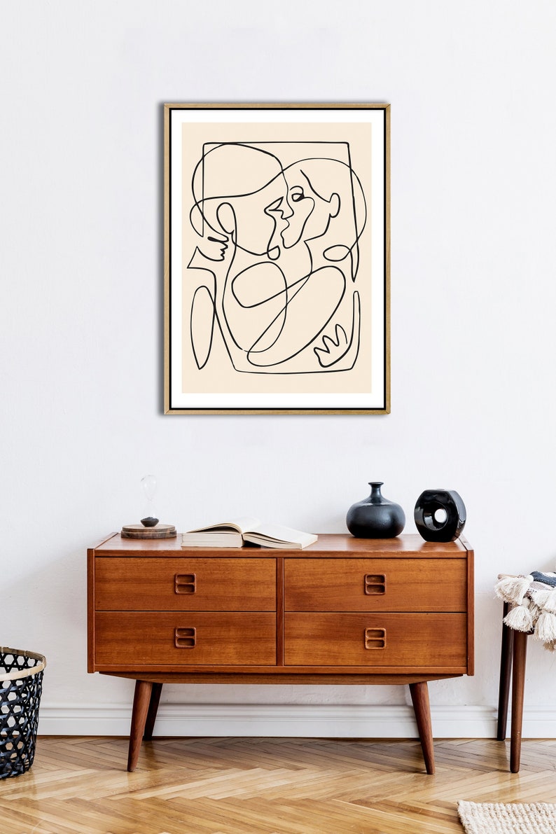 May include: A black and white line drawing of two people embracing, framed in a light wood frame. The drawing is on a cream background.