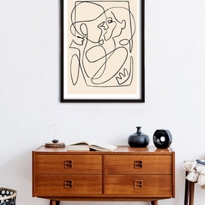 May include: A black and white line drawing of two people embracing, framed in a black frame and hanging on a white wall above a wooden dresser.