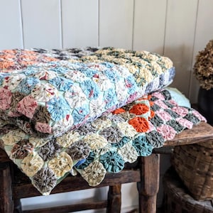 May include: Two vintage quilts made with a unique, hand-stitched, 'penny rug' technique. The quilts are made with a variety of colourful fabrics and feature a floral pattern. The quilts are folded and displayed on a wooden table.