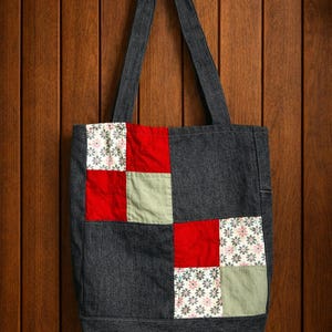 Peut inclure: Un sac fourre-tout en denim avec des carrés patchwork aux motifs rouges, floraux et vert olive. Le sac a une forme rectangulaire avec une poignée en denim assortie.