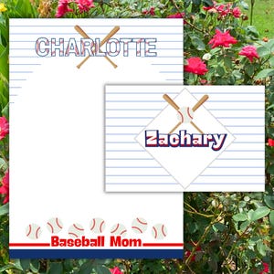 May include: A white stationery set with blue horizontal lines featuring the name Charlotte in blue letters with red stitching detail, crossed baseball bats, and a bottom border of baseballs with the red text Baseball Mom above a navy blue stripe.