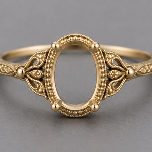 May include: A gold ring setting featuring an oval-shaped center mount with four prongs. The band and the gallery are decorated with intricate metalwork, including beaded edges and openwork filigree patterns along the sides of the ring.