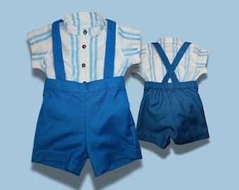 Puede incluir: Conjunto de camisa de manga corta a rayas azules y blancas y pantalón corto azul con tirantes. La camisa tiene cuello mandarín y botones de madera. El pantalón corto es de color azul liso. El conjunto se muestra sobre un fondo azul claro.