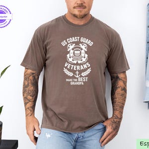 May include: Espresso-colored t-shirt featuring a white graphic that reads "US Coast Guard Veterans Make the Best Grandpa." The design includes an anchor, wreath, and the Coast Guard emblem. The shirt is worn by a person in blue jeans.